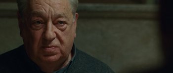 Movie still from “The American” (2010), directed by Anton Corbijn – An older man with a gray beard and a gray sweater; Close Up shot, Over the shoulder angle