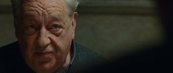 Movie still from “The American” (2010), directed by Anton Corbijn – An old man with a gray beard and a black sweater; Close Up shot, Over the shoulder angle