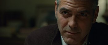 Movie still from “The American” (2010), directed by Anton Corbijn – A person wearing a suit and tie; Close Up shot, Over the shoulder angle