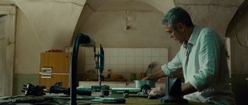 Movie still from “The American” (2010), directed by Anton Corbijn – A man working in a kitchen with a lot of tools on the table; Medium shot, Low angle