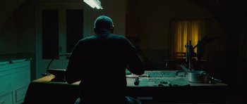 Movie still from “The American” (2010), directed by Anton Corbijn – A man sitting in front of a pool table in a dark room; Medium shot, Low angle