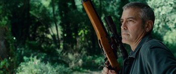 Movie still from “The American” (2010), directed by Anton Corbijn – A man holding a rifle in a wooded area; Close Up shot, Low angle