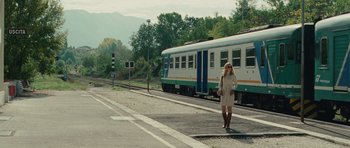 Movie still from “The American” (2010), directed by Anton Corbijn – A woman standing on the side of a road next to a train; Wide shot, Low angle