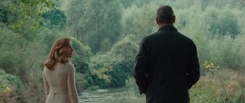 Movie still from “The American” (2010), directed by Anton Corbijn – A man and a woman standing next to each other near a body of water; Medium shot, Over the shoulder angle