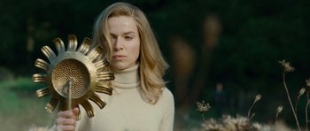 Movie still from “The American” (2010), directed by Anton Corbijn – A woman in a white sweater holding a gold object; Close Up shot, Low angle
