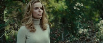 Movie still from “The American” (2010), directed by Anton Corbijn – A woman in a white sweater is standing in a forest; Close Up shot, Low angle