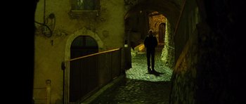 Movie still from “The American” (2010), directed by Anton Corbijn – A man standing in a dark alleyway at night; Wide shot, Low angle