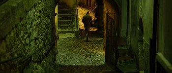 Movie still from “The American” (2010), directed by Anton Corbijn – A man walking down a stone path in an alley way; Wide shot, High angle