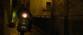 Movie still from “The American” (2010), directed by Anton Corbijn – A person riding a scooter at night on the street; Wide shot, Low angle