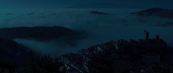 Movie still from “The American” (2010), directed by Anton Corbijn – A view of a town at night with a mountain in the background; Extreme Wide shot, High angle