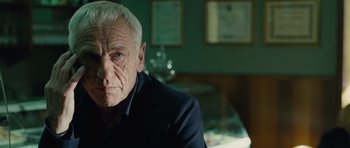 Movie still from “The American” (2010), directed by Anton Corbijn – An older man sitting at a table in front of a mirror; Close Up shot, Over the shoulder angle