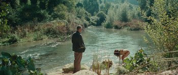 Movie still from “The American” (2010), directed by Anton Corbijn – A man standing next to a body of water; Extreme Wide shot, High angle