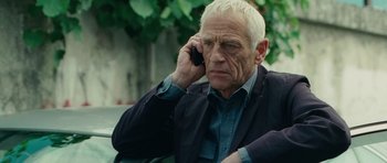 Movie still from “The American” (2010), directed by Anton Corbijn – An older man talking on a cell phone while sitting outside; Close Up shot, Over the shoulder angle