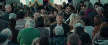 Movie still from “The American” (2010), directed by Anton Corbijn – A crowd of people standing in a room; Medium shot, Over the shoulder angle