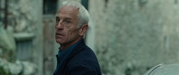 Movie still from “The American” (2010), directed by Anton Corbijn – An older man with white hair and blue eyes looking at the camera; Close Up shot, Over the shoulder angle