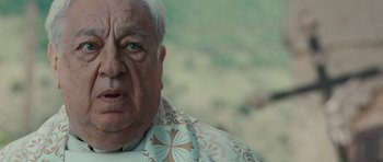 Movie still from “The American” (2010), directed by Anton Corbijn – An old man with a white beard and a blue and white shirt; Close Up shot, Over the shoulder angle