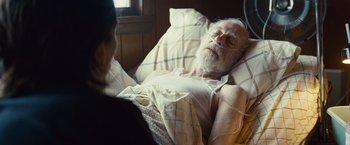 Movie still from “Out of the Furnace” (2013), directed by Scott Cooper – An older man laying in a bed with a woman looking at him; Medium shot, High angle