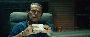 Movie still from “Out of the Furnace” (2013), directed by Scott Cooper – A man sitting in a chair holding a piece of paper in front of him; Close Up shot, Low angle