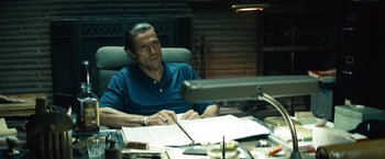 Movie still from “Out of the Furnace” (2013), directed by Scott Cooper – A man sitting in front of a computer desk; Medium shot, Low angle