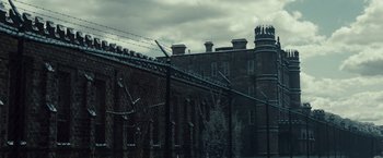 Movie still from “Out of the Furnace” (2013), directed by Scott Cooper – A brick building with barbed wire on top of it; Extreme Wide shot, Low angle