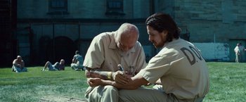Movie still from “Out of the Furnace” (2013), directed by Scott Cooper – Two men sitting on the ground with tattoos on their arms; Medium shot, Low angle