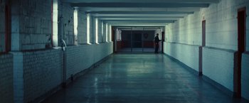 Movie still from “Out of the Furnace” (2013), directed by Scott Cooper – A person standing in a hallway with a door open; Extreme Wide shot, High angle