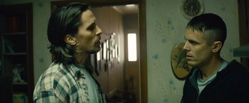 Movie still from “Out of the Furnace” (2013), directed by Scott Cooper – A man standing next to a mirror in a room; Medium shot, Over the shoulder angle