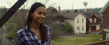 Movie still from “Out of the Furnace” (2013), directed by Scott Cooper – A woman in a plaid shirt standing in front of a house; Close Up shot, Over the shoulder angle