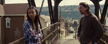 Movie still from “Out of the Furnace” (2013), directed by Scott Cooper – A woman standing on top of a metal fence; Medium shot, Over the shoulder angle