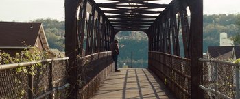 Movie still from “Out of the Furnace” (2013), directed by Scott Cooper – A person standing on a bridge holding a frisbee; Extreme Wide shot, High angle