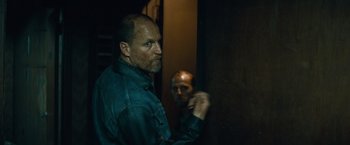 Movie still from “Out of the Furnace” (2013), directed by Scott Cooper – A man standing next to another man in a dark room; Close Up shot, Over the shoulder angle