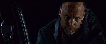 Movie still from “Out of the Furnace” (2013), directed by Scott Cooper – A man with a beard and a leather jacket on; Close Up shot, Low angle