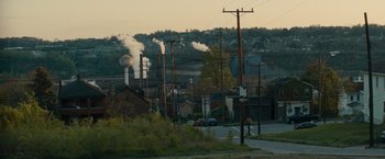 Movie still from “Out of the Furnace” (2013), directed by Scott Cooper – Smoke billows from a factory in a rural area; Extreme Wide shot, High angle