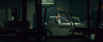 Movie still from “Out of the Furnace” (2013), directed by Scott Cooper – A man sitting at a desk in front of a computer; Wide shot, High angle