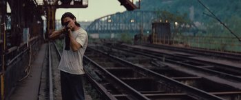 Movie still from “Out of the Furnace” (2013), directed by Scott Cooper – A man standing next to train tracks while talking on a cell phone; Medium shot, Over the shoulder angle