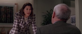 A woman in a plaid jacket looking at a man in a suit in front of a mirror