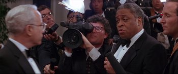 Movie still from “The American President” (1995), directed by Rob Reiner – A group of people standing around a man holding a video camera; Close Up shot, Low angle