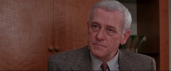 Movie still from “The American President” (1995), directed by Rob Reiner – An older man wearing a suit and tie in front of a wooden cabinet; Close Up shot, Low angle