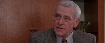 Movie still from “The American President” (1995), directed by Rob Reiner – An older man wearing a suit and tie in front of a wooden wall; Close Up shot, Low angle