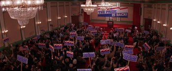 Movie still from “The American President” (1995), directed by Rob Reiner – A crowd of people holding up signs in a room; Extreme Wide shot, High angle