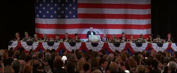 Movie still from “The American President” (1995), directed by Rob Reiner – A group of people sitting at a table in front of an american flag; Wide shot, High angle