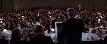 Movie still from “The American President” (1995), directed by Rob Reiner – A crowd of people sitting at tables and a man standing at a microphone; Medium shot, High angle