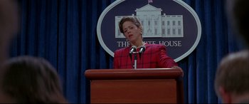 Movie still from “The American President” (1995), directed by Rob Reiner – A woman in a red plaid jacket is speaking at a podium; Medium shot, Low angle