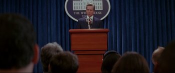 Movie still from “The American President” (1995), directed by Rob Reiner – A man in a suit and tie at a press conference; Medium shot, Low angle