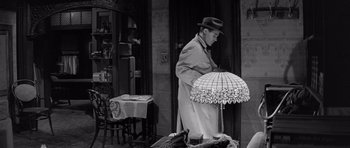 Movie still from “The Apartment” (1960), directed by Billy Wilder – A man standing in front of a table with a lamp; Medium shot, High angle