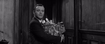 Movie still from “The Apartment” (1960), directed by Billy Wilder – A black and white photo of a man holding a cage; Medium shot, Low angle
