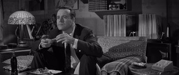 Movie still from “The Apartment” (1960), directed by Billy Wilder – A black and white photo of a man sitting on a couch; Medium shot, Low angle
