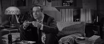 Movie still from “The Apartment” (1960), directed by Billy Wilder – A black and white photo of a man sitting on a couch; Medium shot, Low angle