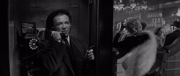 Movie still from “The Apartment” (1960), directed by Billy Wilder – An old man talking on a phone next to a woman holding a cell phone; Medium shot, Low angle