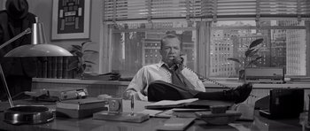 Movie still from “The Apartment” (1960), directed by Billy Wilder – A man sitting at a desk talking on the phone; Medium shot, Low angle